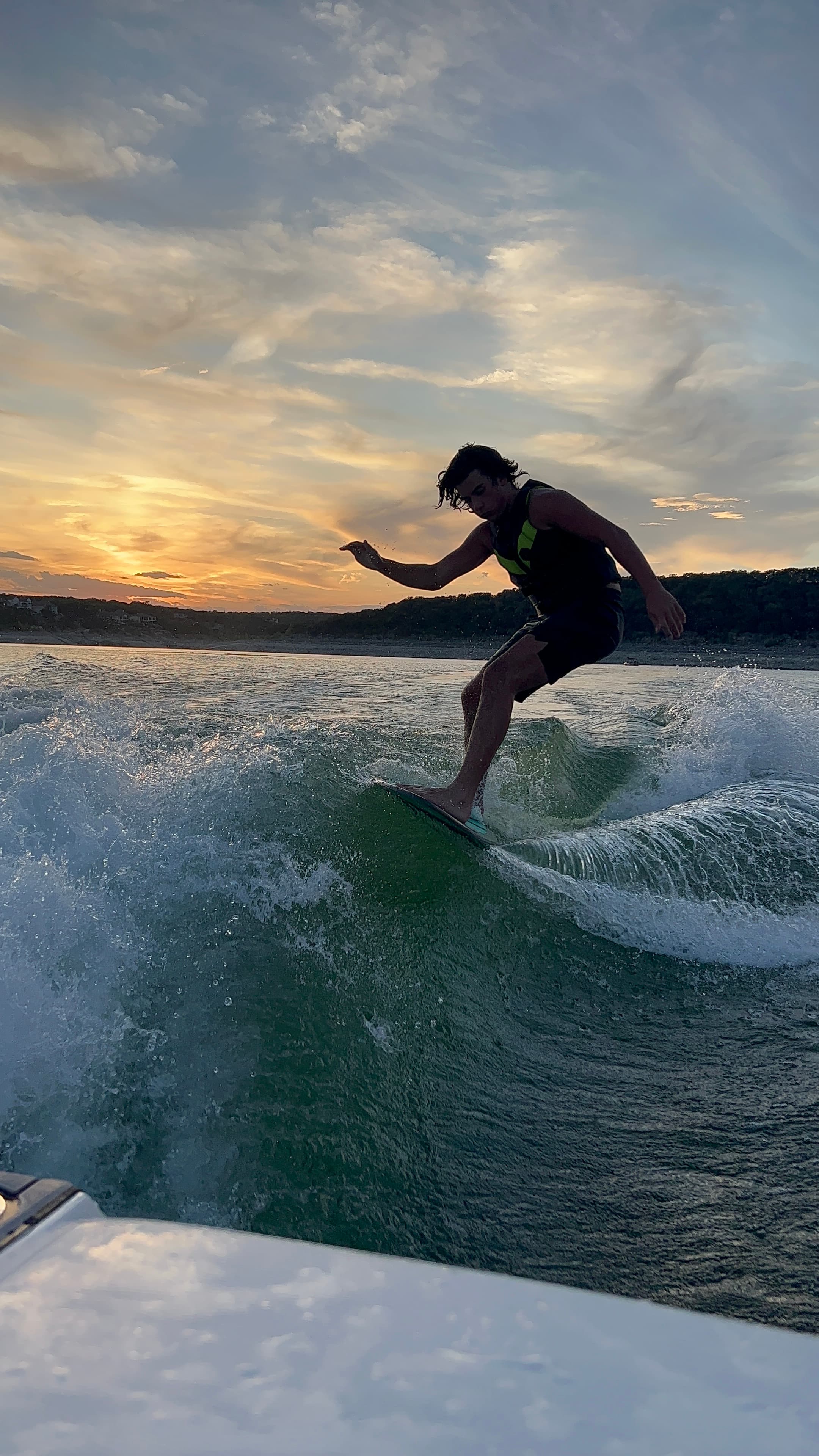 A rider carving the wake behind the boat on Lake Travis at sunset.